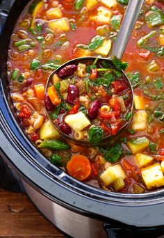 a ladle full of vegetable soup in a crock pot on top of a wooden table