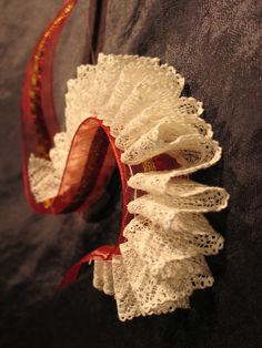 a white lace garter with red ribbon hanging from it's side on a black background