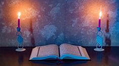 an open book sitting on top of a table next to two lit candles