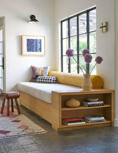 a living room filled with furniture and flowers on top of a wooden shelf next to a window