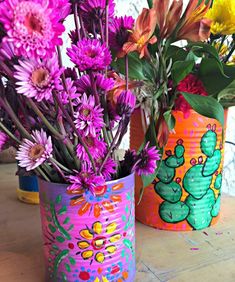 two tin cans with flowers in them sitting on a table next to another container filled with flowers