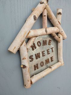 a home sweet home sign hanging on the side of a house made out of wood sticks