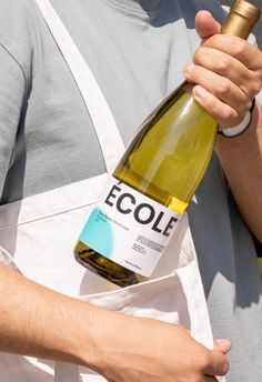 a man holding a bottle of wine in his hand and wearing an apron with the word ecolie printed on it