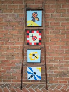 three paintings are hanging on a brick wall next to a ladder that is leaning against the wall