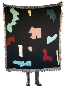 a woman holding up a black blanket with multicolored shapes and fringes on it