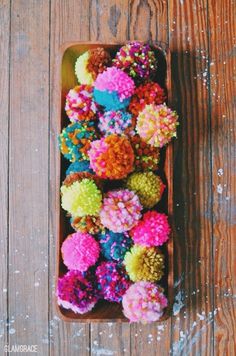 an overhead view of colorful pom - poms in a tray on a wooden surface