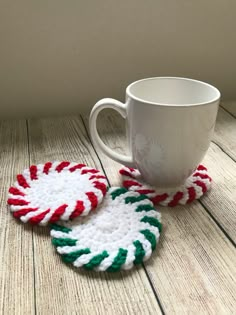 two crocheted candy cane coasters sitting next to a coffee cup