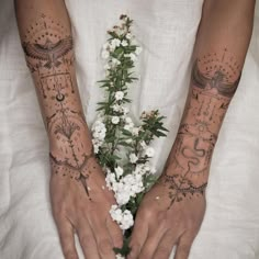 two hands with tattoos and flowers on their palms, both holding each other's arms