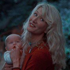 a woman holding a baby in her arms and looking up at the sky with one eye open