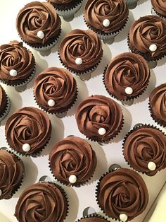 cupcakes with chocolate frosting and pearls are arranged in a box