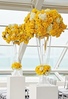 yellow and white flowers are arranged in vases on pedestals at the reception table