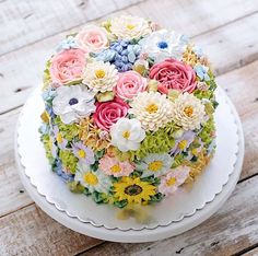 a cake decorated with flowers sitting on top of a white plate and wooden flooring