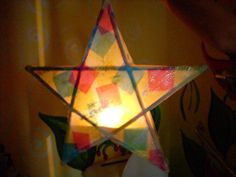 a person holding a lit candle in front of a stained glass star ornament