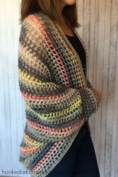 a woman wearing a multicolored crochet cardigan standing in front of a white wall