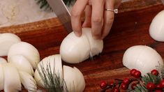 a person cutting onions on a wooden board with a knife and holly wreath around them