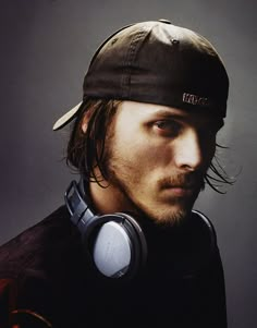 a man with long hair wearing headphones and a cap is looking at the camera