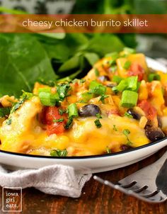 a white bowl filled with cheesy chicken burrito skillet on top of a wooden table