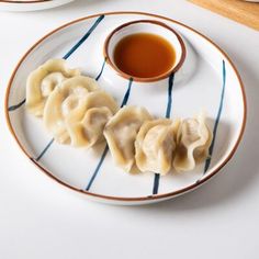 dumplings on a plate with dipping sauce in the middle and another dish next to it