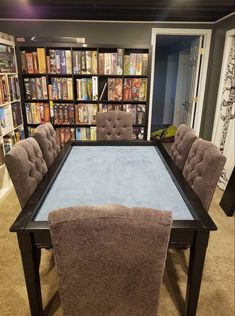 a table with several chairs around it in front of a bookcase filled with books