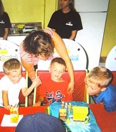 a woman bending over to blow out candles on a birthday cake with kids around her