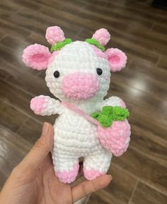 a hand holding a small white and pink crocheted cow with green leaves on its head