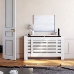 a white cabinet sitting on top of a hard wood floor next to a wall mounted painting