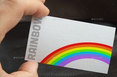 a person holding up a business card with a rainbow on the front and bottom corner