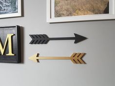 three metal arrows are hanging on the wall next to two framed pictures and one is gold