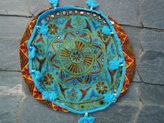 a colorful round bag with tassels and beads on the bottom sitting on a stone surface