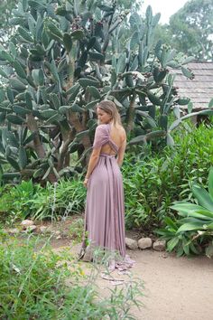 a woman in a long dress standing next to a cactus tree and looking off into the distance