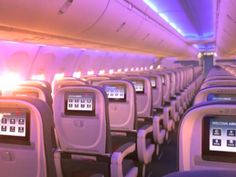 the inside of an airplane with rows of seats and electronic screens on the back wall