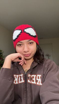 a young woman wearing a red and white knitted hat sitting in front of a christmas tree