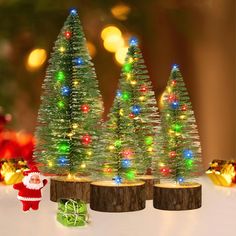 three small christmas trees with lights on them and a santa clause figure next to it