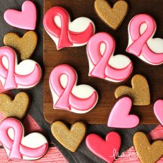 pink and gold decorated cookies with hearts on a wooden board next to other heart shaped cookies