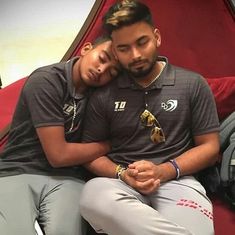 two people sitting next to each other in front of a red couch with their arms around one another