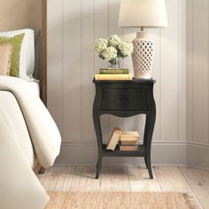 a night stand with flowers and books on it next to a bed in a bedroom