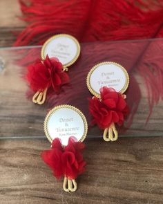 three small red flowers with gold trims on top of a wooden table next to feathers