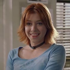 a woman with red hair wearing a blue shirt and black choker smiling at the camera