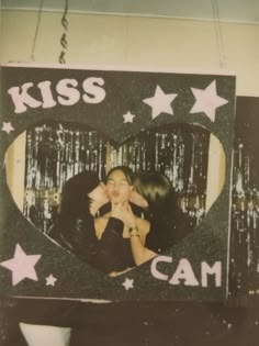 two women kissing in front of a sign that says kiss cam and stars hanging from the ceiling