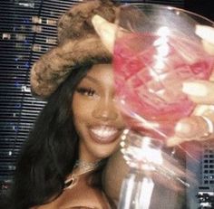 a woman wearing a hat holding a wine glass in front of a cityscape