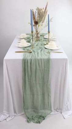 the table is set with white and green linens, gold place settings and tall blue candlesticks