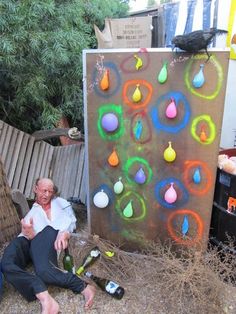 a man sitting on the ground in front of a wall with colorful drops painted on it