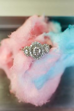 an engagement ring sitting on top of a pile of pink and blue fluffy material in front of a mirror