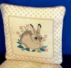 a cross stitch pillow with a bunny on it's side and a blue wall in the background