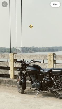 a black motorcycle parked on the side of a road next to a wooden fence and water