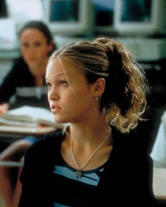 a woman sitting at a desk in front of a computer monitor with another person behind her