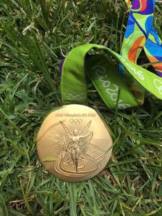 a gold medal laying in the grass next to a green ribbon