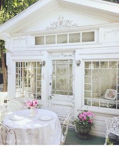 a table and chairs in front of a small white house with flowers on the outside