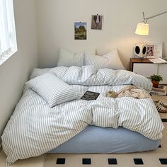 an unmade bed with blue and white striped comforter in a small room next to a window