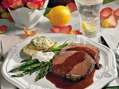 a white plate topped with meat and asparagus next to a glass of water